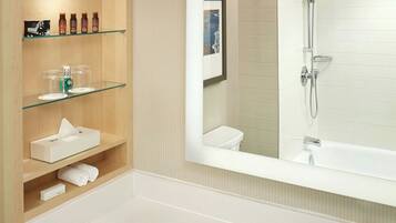 A modern bathroom with a large sink, a mirror, and a shower. There are shelves with toiletries and towels.