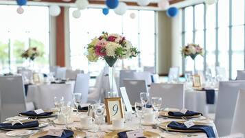 Een feesttafel gedekt met witte tafelkleden, gouden en marineblauwe servetten, en genummerde zitplaatskaarten.