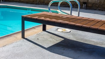Un fauteuil de relaxation en bois placé près d’une piscine, avec une échelle en métal et un sol en béton.