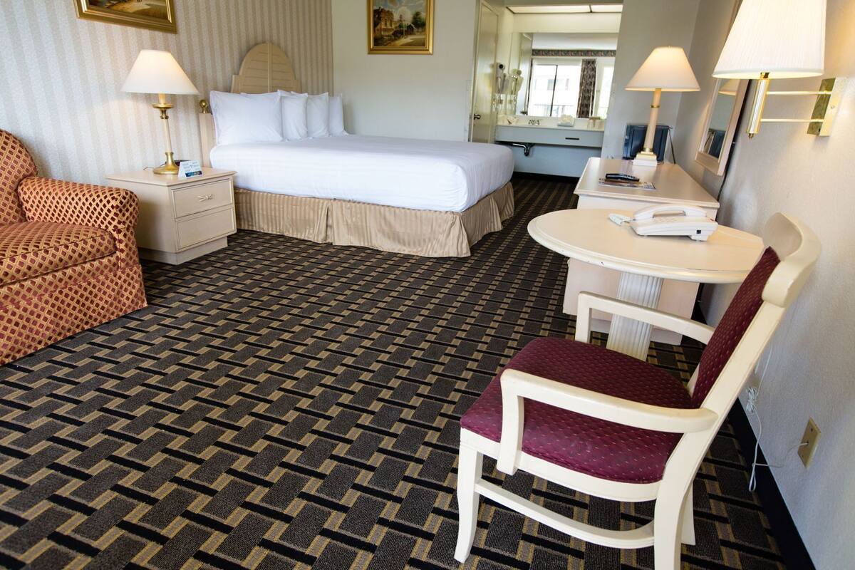 A hotel room with a bed, a desk with a chair, a small table, and a sofa.