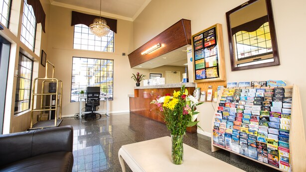 A spacious lobby with a reception desk, a coffee machine, a bulletin board with travel brochures, and a vase with flowers. - Anaheim Carriage Inn (Anaheim)