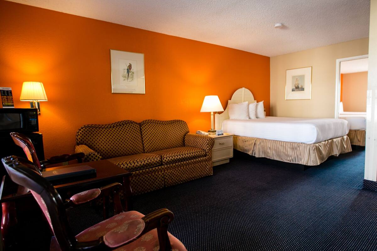 A hotel room with a bed, a sofa, a desk with a lamp, and a chair.