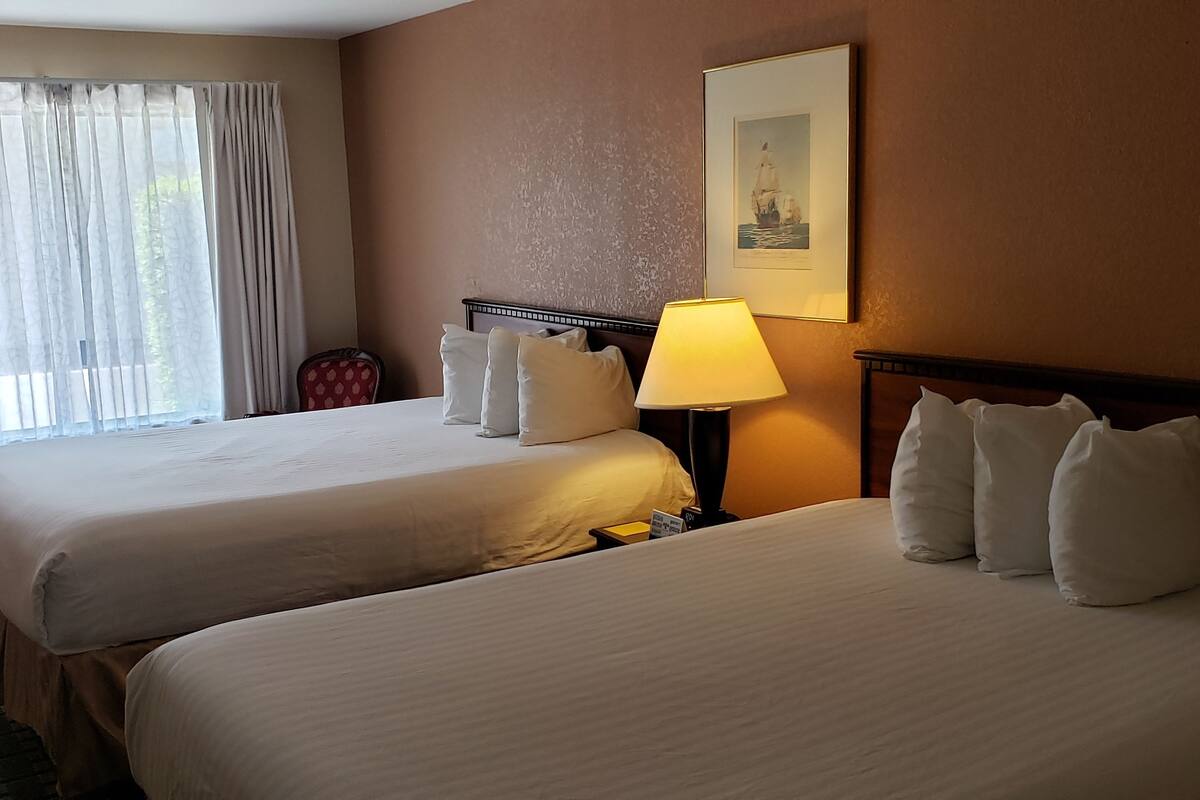 A hotel room with two beds, a lamp, a chair, and a window with curtains.