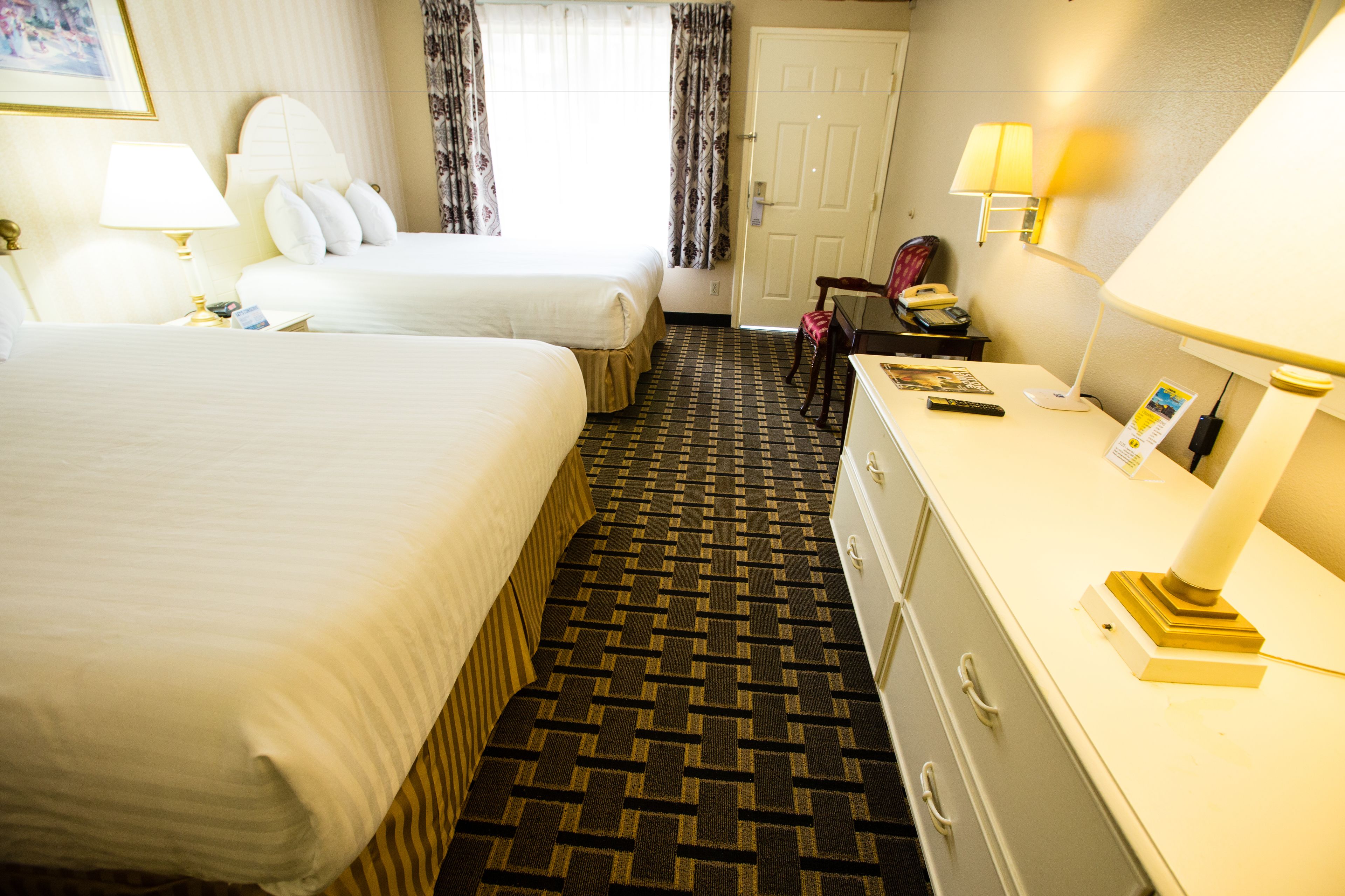 A hotel room with two beds, a desk with a lamp, a chair, and a dresser.