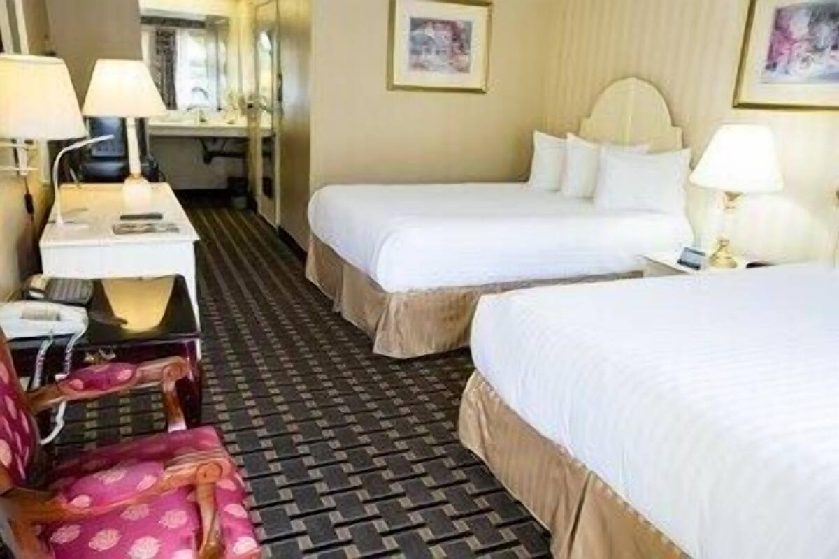 A hotel room with two beds, a desk, a chair, and a patterned floor.
