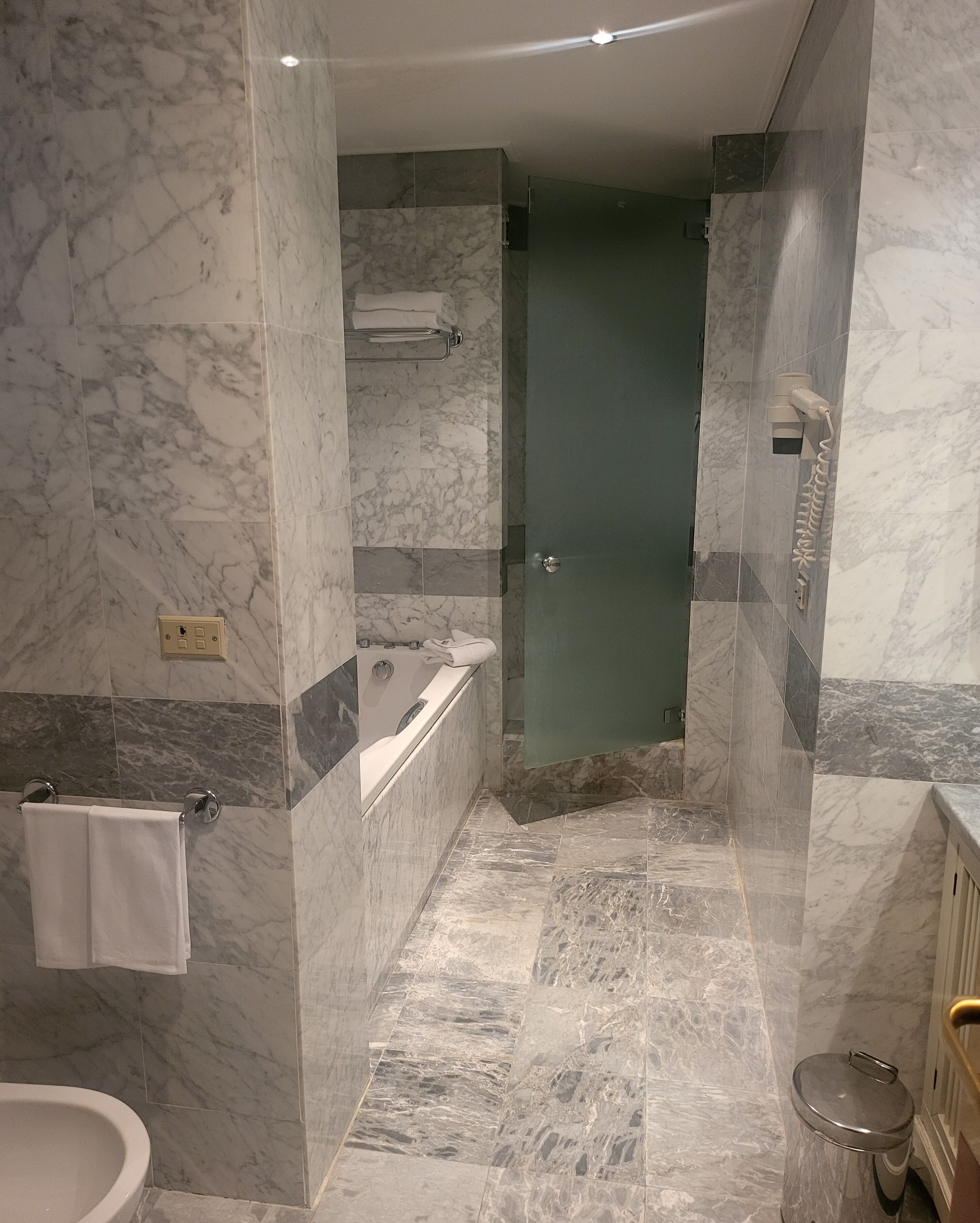A modern bathroom with a marble floor, a bathtub, a shower, and a toilet.