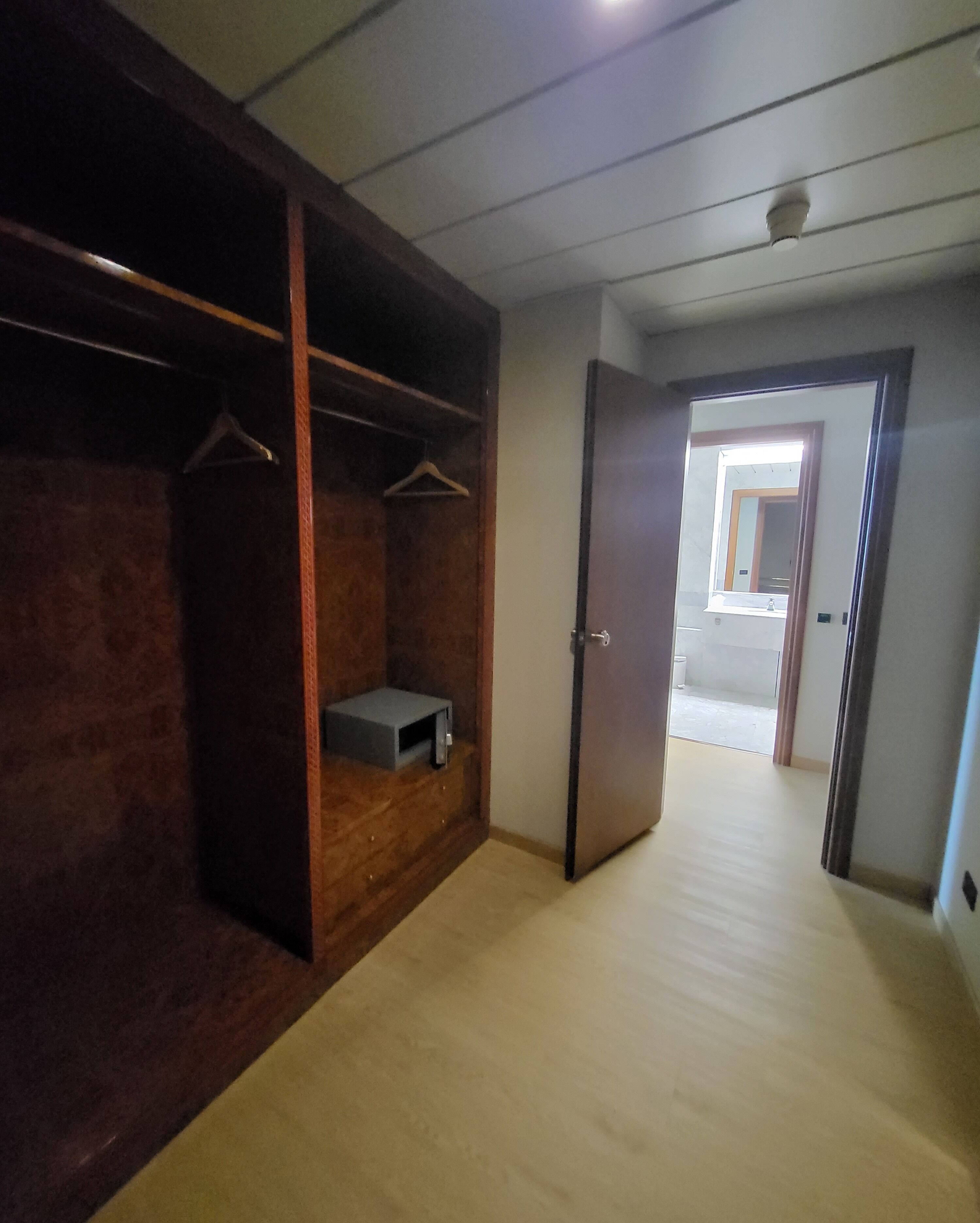 Een kamer met een houten garderobe, een klein plankje en een deur naar een andere kamer.
