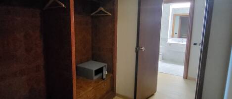 A room with a wooden wardrobe, a small shelf, and a door leading to another room.