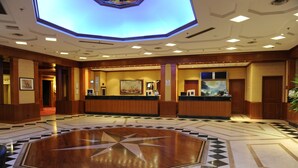 A hotel lobby with a large central star-shaped floor design, wooden reception desks, and a ceiling with recessed lighting. - Tower Genova Airport Hotel & Conference Center (Genoa)