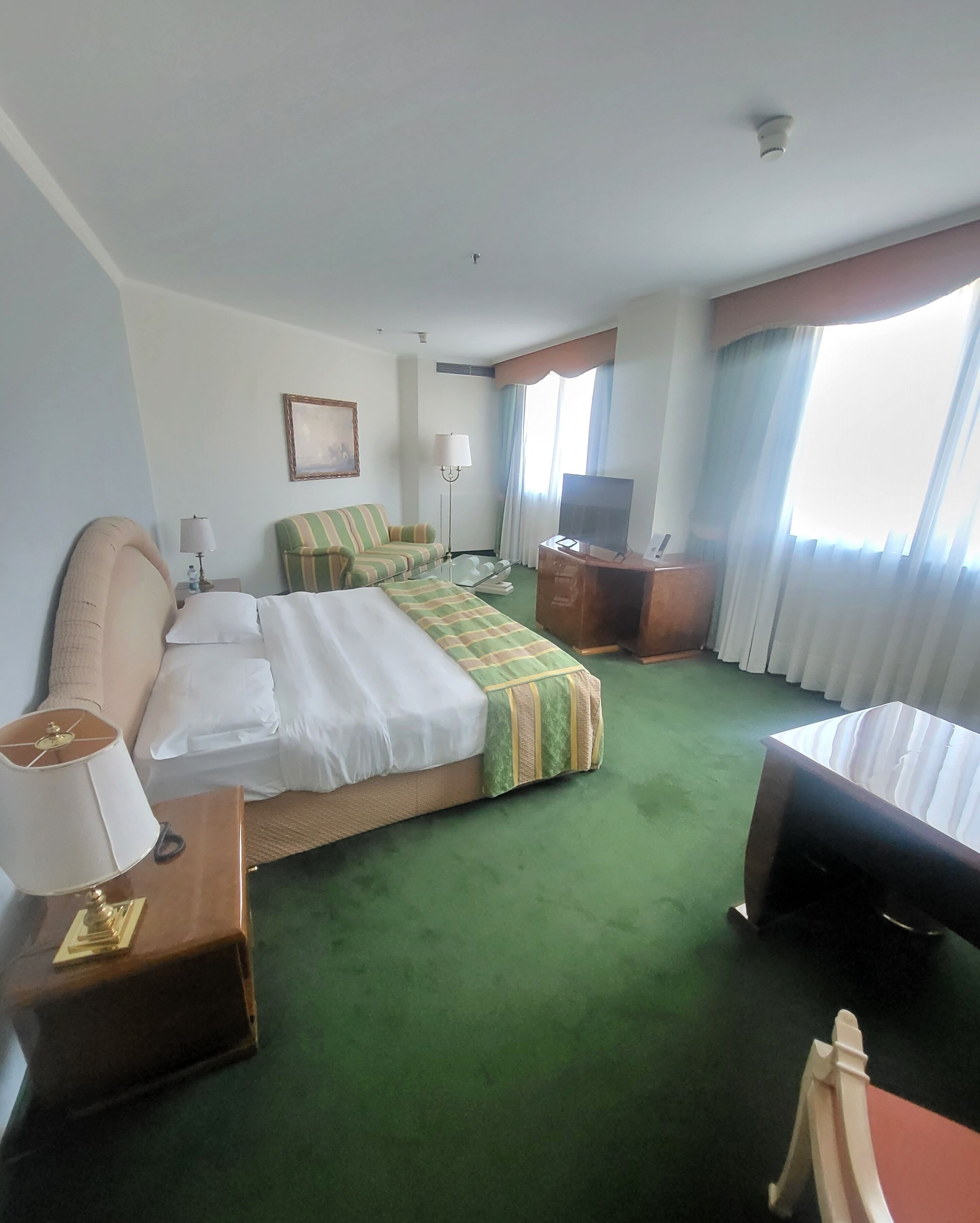 A hotel room with a large bed, a desk with a lamp, a television, and a chair.
