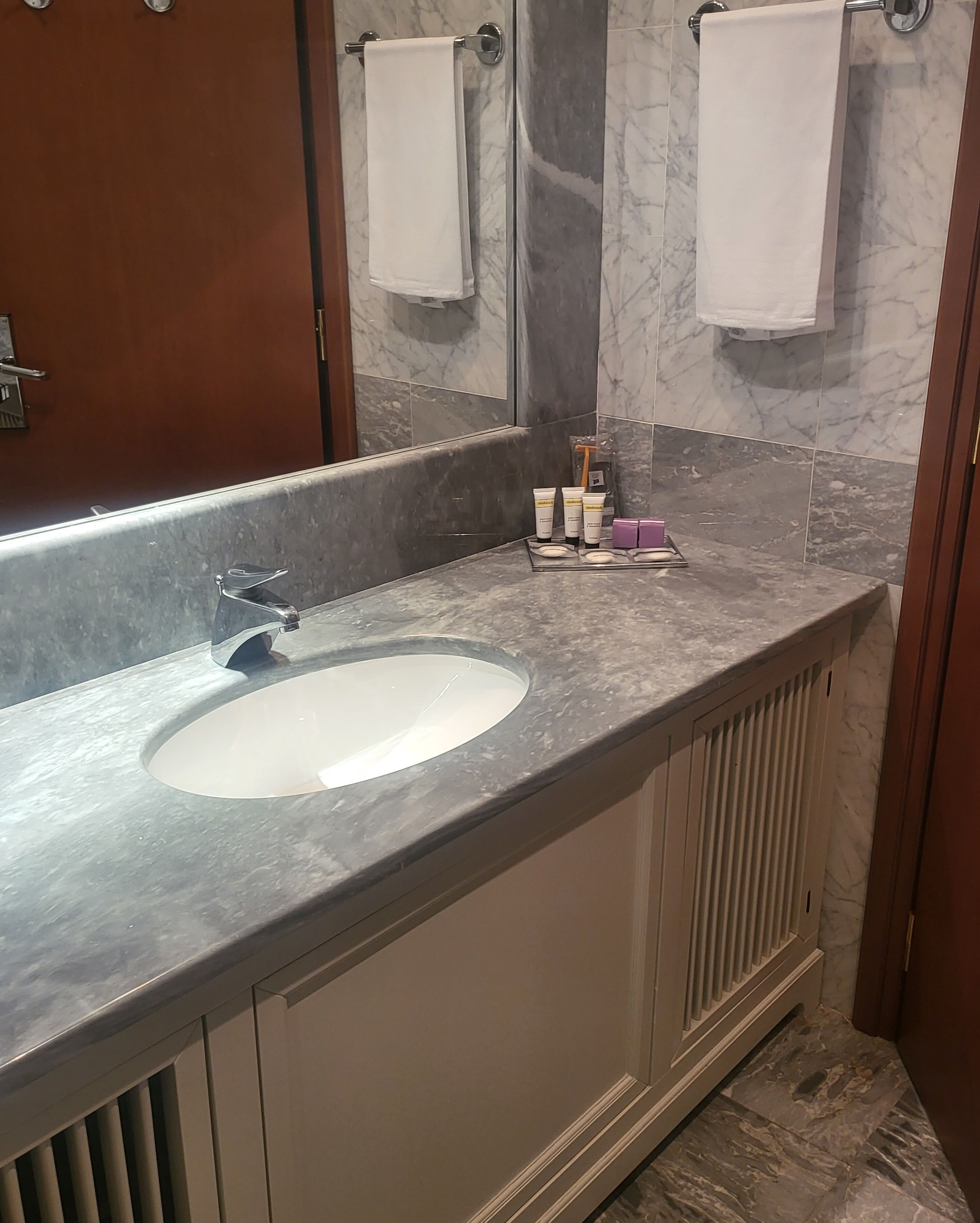 A bathroom with a marble sink, a large mirror, and a towel rack.