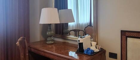 Habitación de hotel con escritorio de madera, dos lámparas, un espejo, una silla, una cama y un cesto de basura.