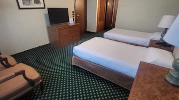 A hotel room with two beds, a desk, a chair, a television, and a framed picture on the wall.