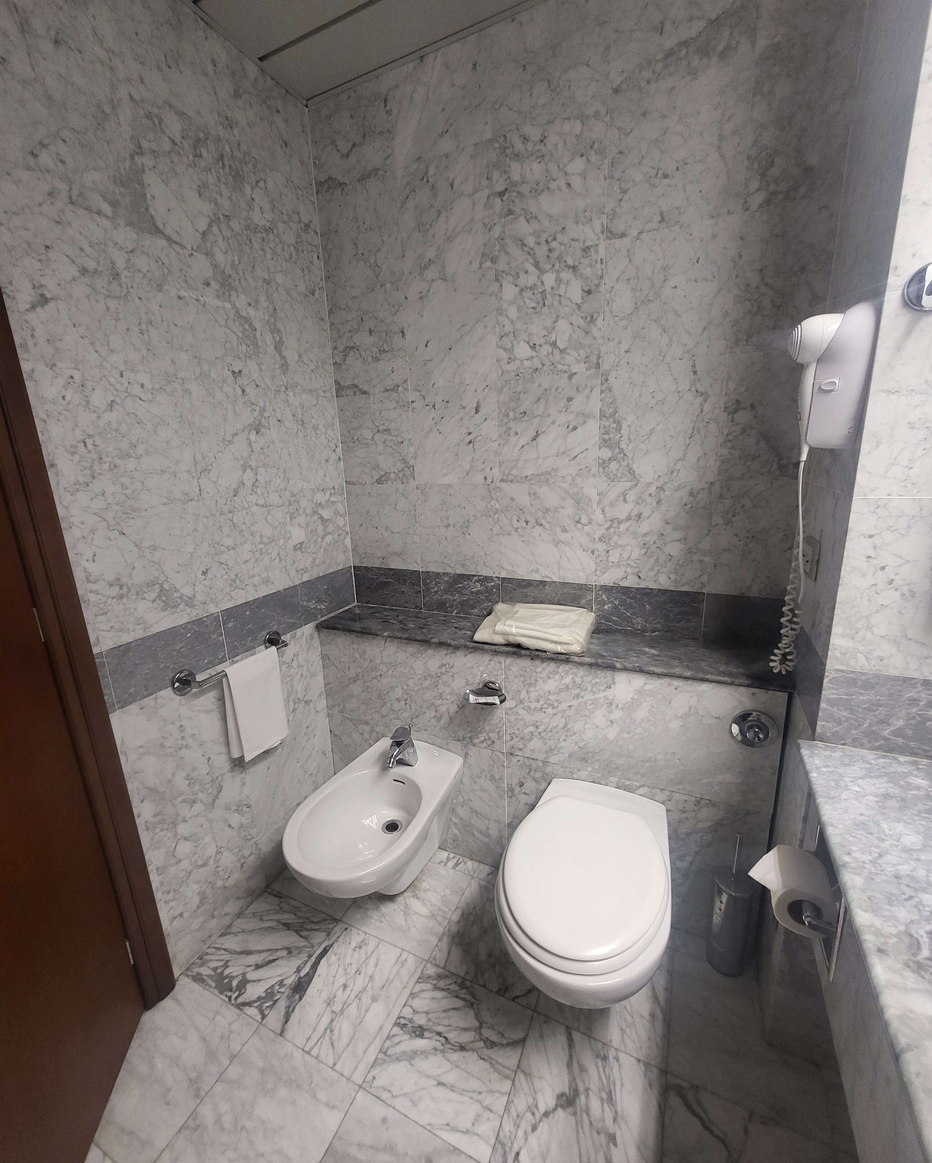 A bathroom with a bidet, toilet, and a hairdryer on a counter.