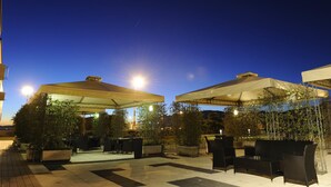 An outdoor patio area with tables and chairs under large umbrellas, surrounded by potted plants. - Tower Genova Airport Hotel & Conference Center (Genoa)
