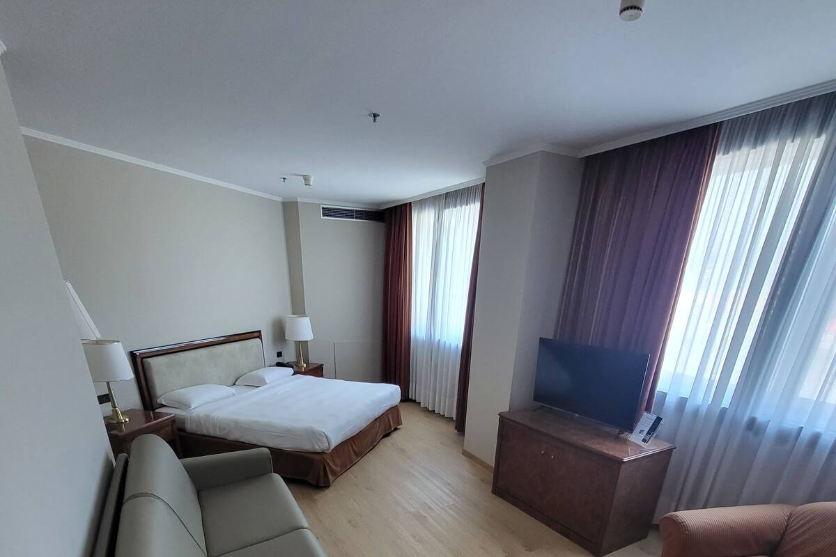 A modern hotel room with a bed, sofa, TV, and a desk.