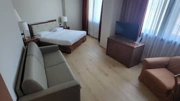 A modern hotel room with a bed, sofa, TV, and a desk.