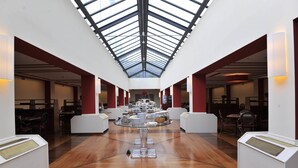 A spacious atrium with a high ceiling and skylight, featuring a central round table with food and drinks, surrounded by seating areas. - Tower Genova Airport Hotel & Conference Center (Genoa)