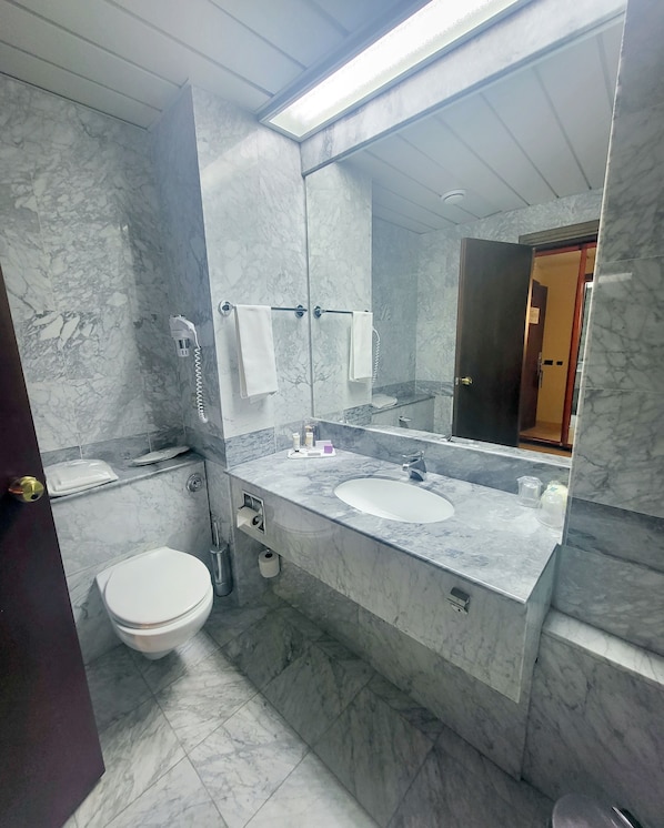 A modern bathroom with a marble sink, a toilet, and a large mirror.