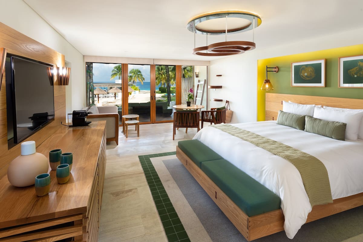 Une chambre d’hôtel moderne dotée d’un grand lit, d’un bureau en bois, d’une télévision et offrant une vue sur la plage.