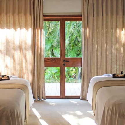 A hotel room with two beds, a large sliding glass door leading to a balcony with a view of palm trees.