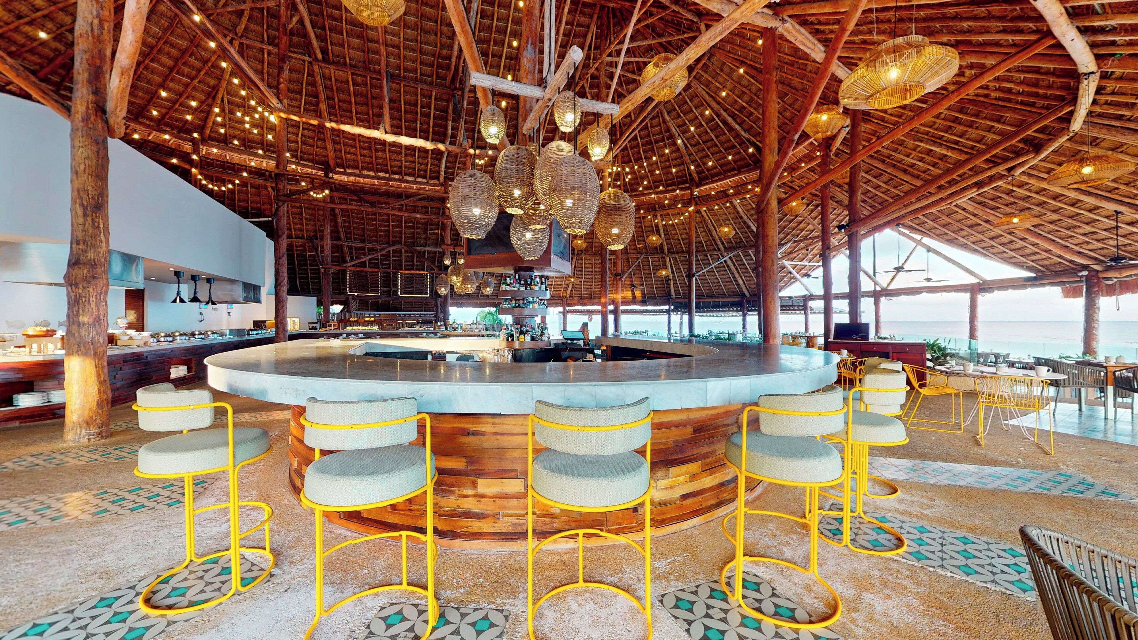 A spacious bar area with a central island, high wooden ceiling, and hanging wicker lamps.