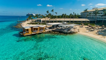 A beachfront hotel with overwater bungalows, a pool, and a beach area with umbrellas.