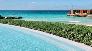 Une piscine à l’eau d’un bleu cristallin, une plage à l’eau turquoise et une structure en bois avec des sièges.