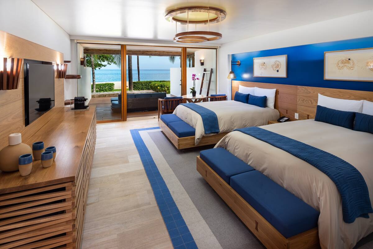 Une chambre d’hôtel moderne avec deux lits, une télévision, un bureau en bois et une vue sur l’océan.
