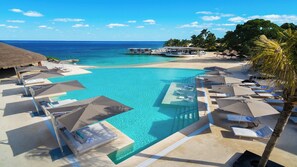 A resort pool with lounge chairs and umbrellas, a beach area with a boat, and a clear view of the ocean. - InterContinental Presidente Cozumel Resort Spa by IHG (Cozumel)
