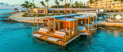 An overwater bungalows with clear blue water, wooden deck, and lounge chairs.