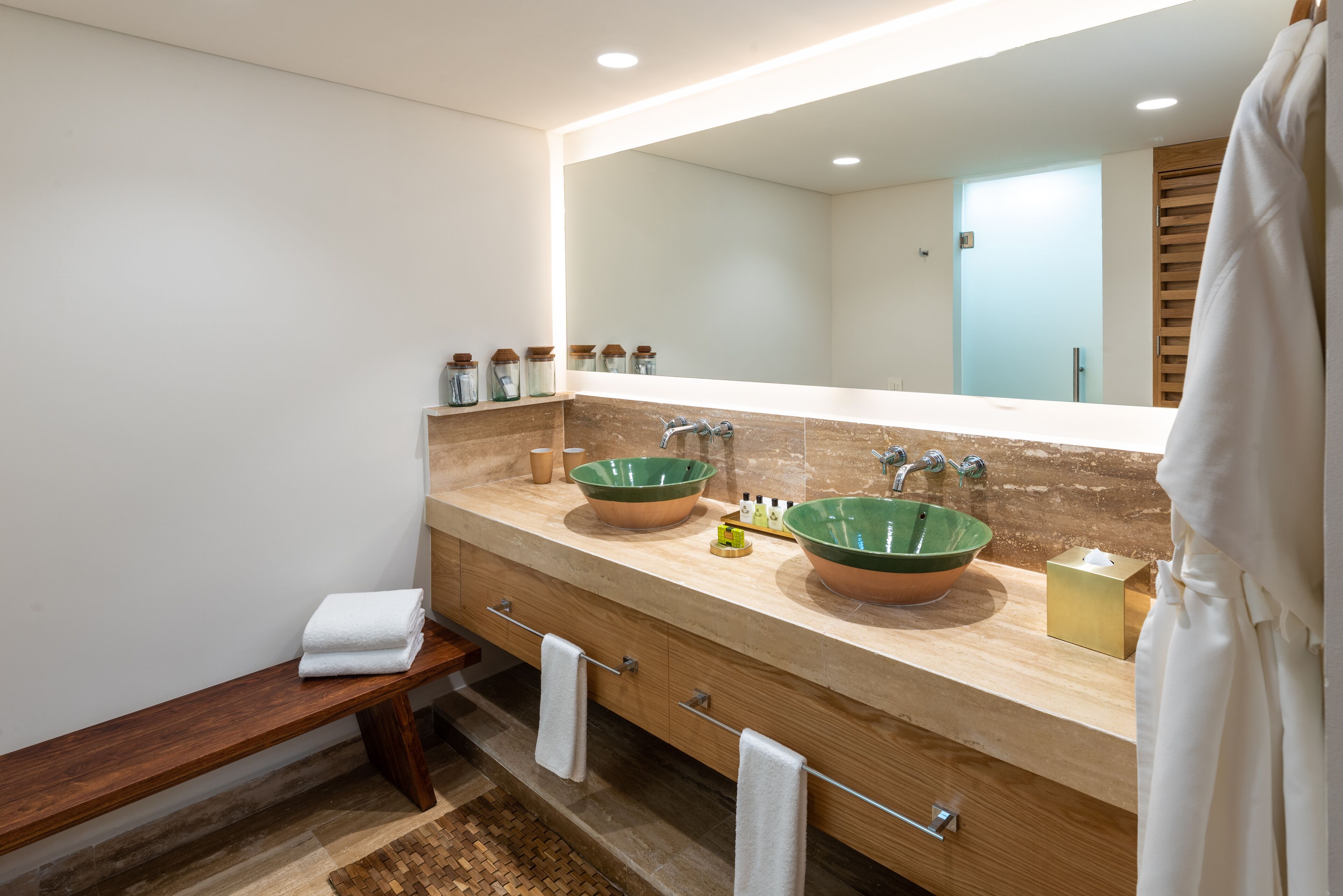 A modern bathroom with two large green ceramic sinks, a wooden bench, and a large mirror.