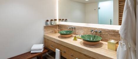 A modern bathroom with two large green ceramic sinks, a wooden bench, and a large mirror.