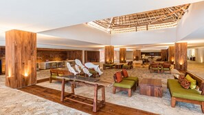 Een ruime lobby met houten details, een hoge plafond en een centraal zitgedeelte met tafels en stoelen.