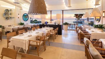 A restaurant with tables set for dining, a view of the sea, and a hanging light fixture.