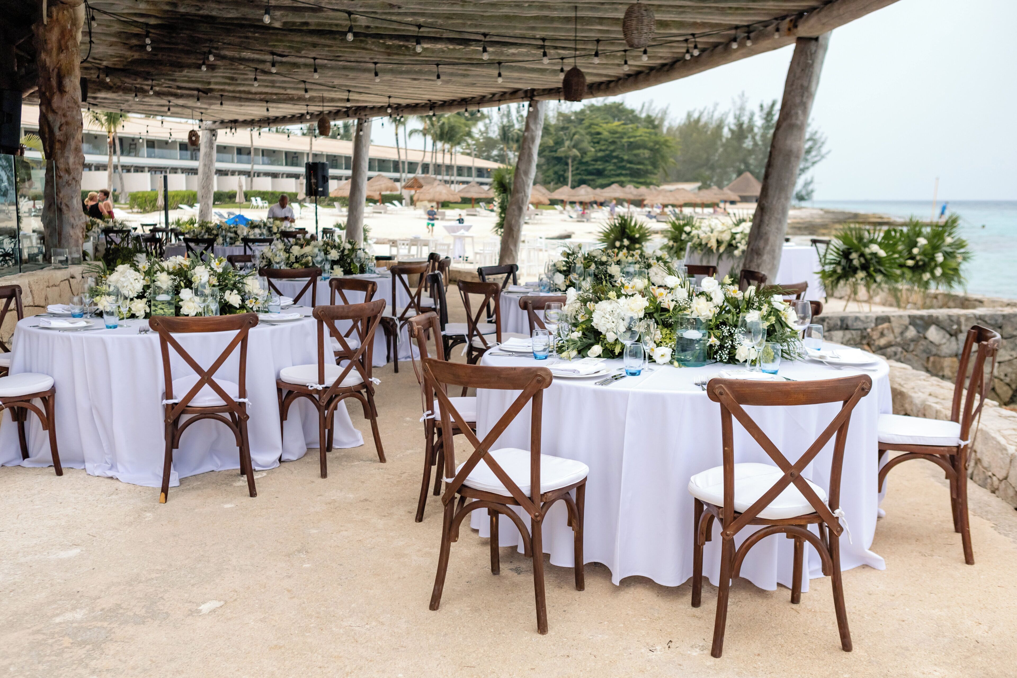 Un área de comedor al aire libre con mesas redondas, manteles blancos y sillas de madera.