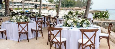 Un área de comedor al aire libre con mesas redondas, manteles blancos y sillas de madera.