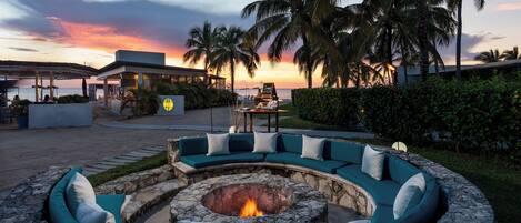 A circular outdoor seating area with a fire pit, surrounded by a stone wall and a curved green sofa with white cushions.