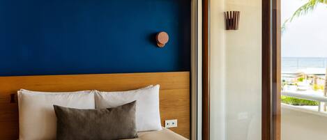 A hotel room with a bed, a wooden headboard, a blue accent wall, and a view of the ocean through a glass door.