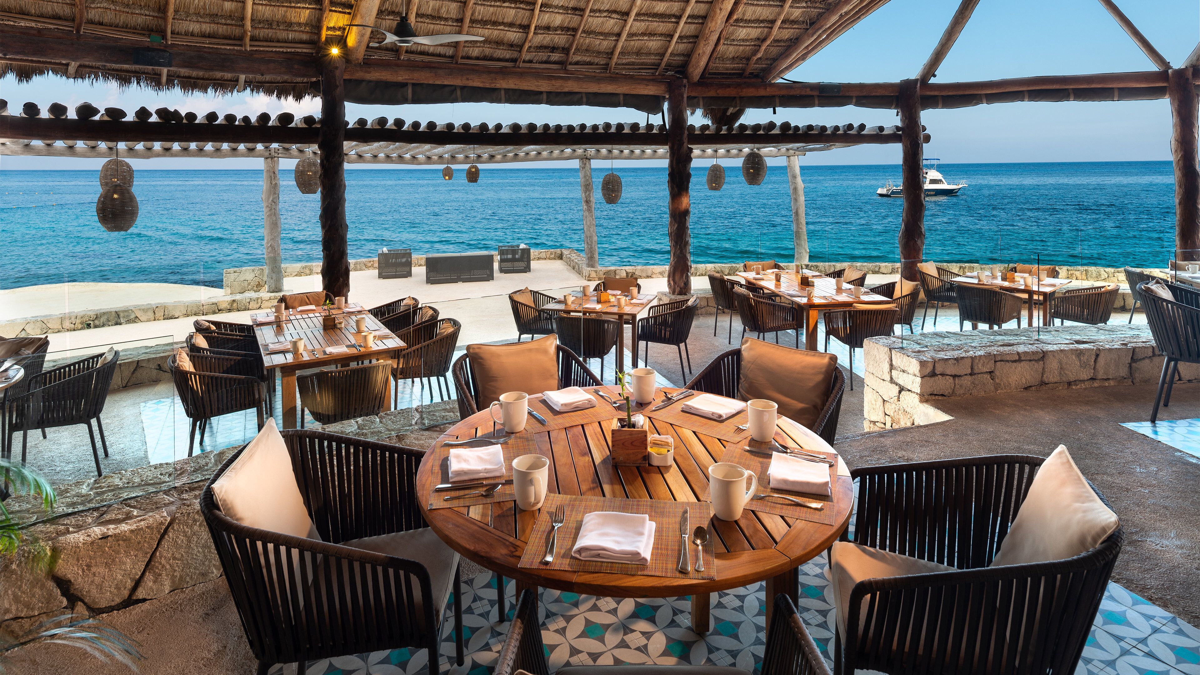 Un área de comedor al aire libre con mesas y sillas, con vista al mar.