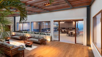 Un espacio interior amplio con piso de madera, una zona de estar con sofás y mesas, ventanas grandes y vista a un comedor.