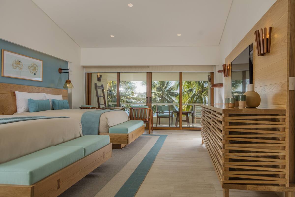 Une chambre moderne avec un grand lit, un canapé, un bureau et un balcon offrant une vue sur les palmiers.