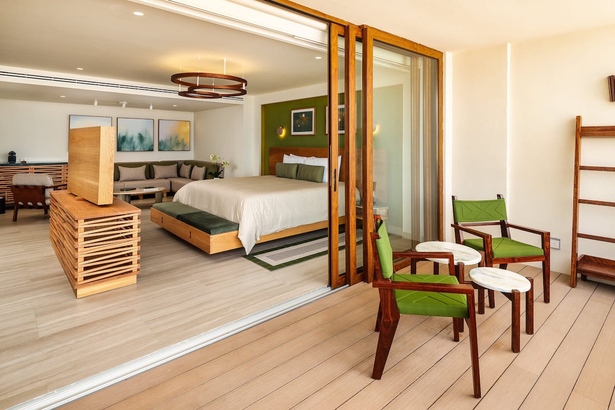 Une chambre d’hôtel moderne avec un grand lit, un banc en bois et un coin salon avec des fauteuils.