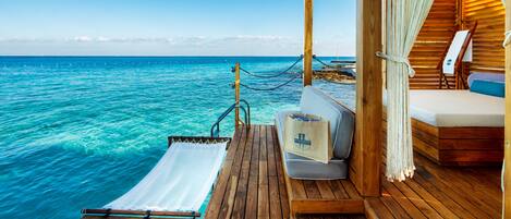 Une terrasse en bois avec une serviette blanche, un sac et un lit avec un oreiller bleu.