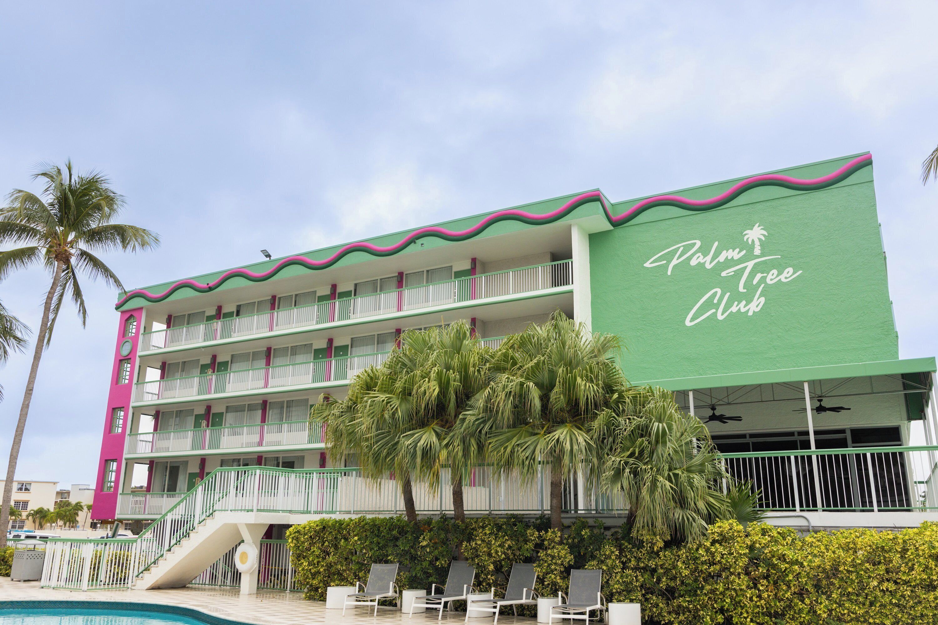A multi-story hotel with balconies, a pool area, and palm trees.