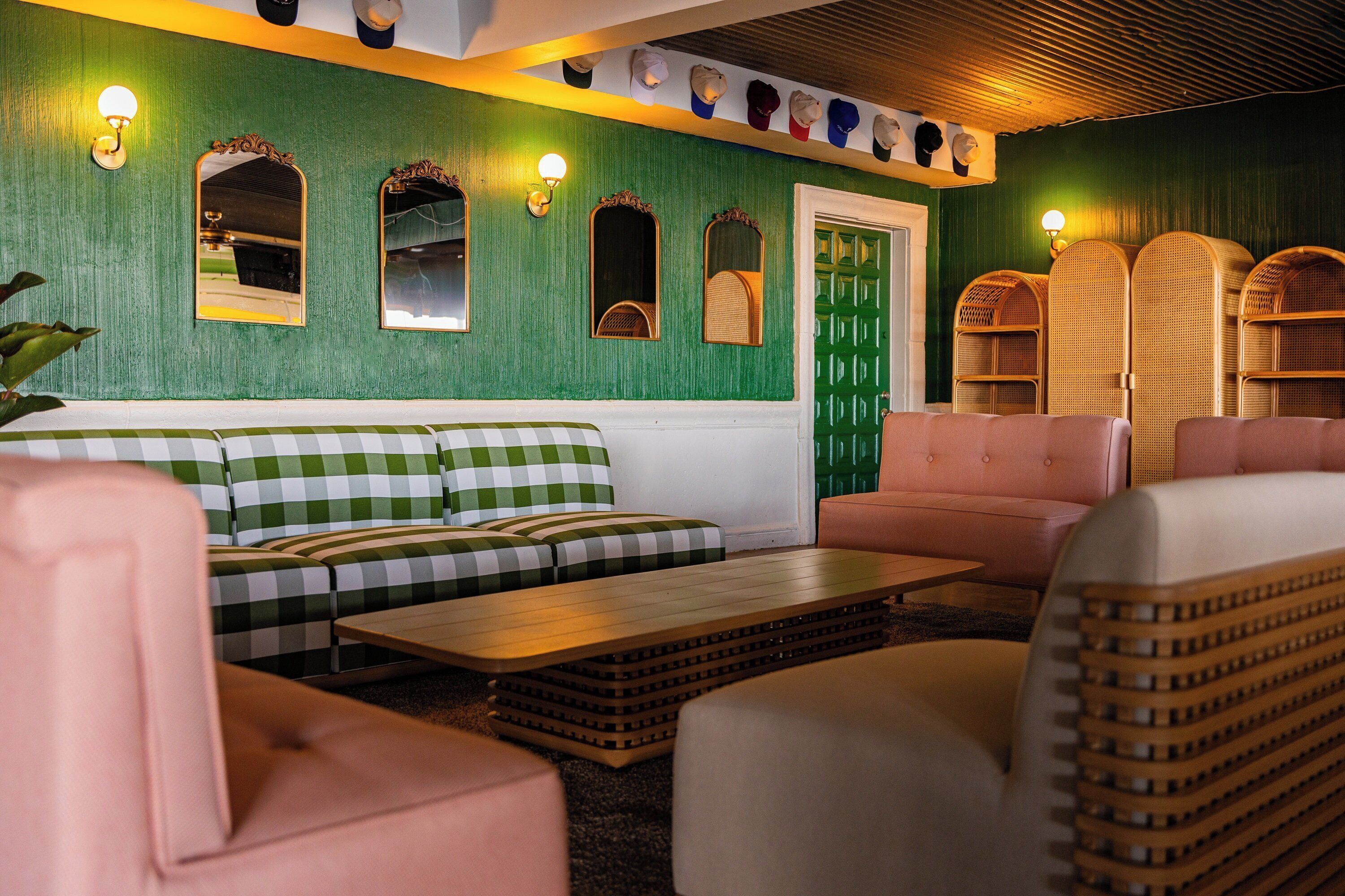 Una habitación con una pared verde, un sofá estampado de cuadros, una mesa de centro de madera y sillas de mimbre.