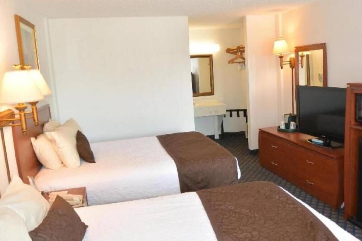 A hotel room with two beds, a desk, a television, and a mirror.