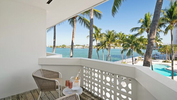 A balcony with wicker chairs, a small table with a bottle and glasses, and a view of the sea and palm trees. - Palm Tree Club Miami Hotel (North Bay Village)
