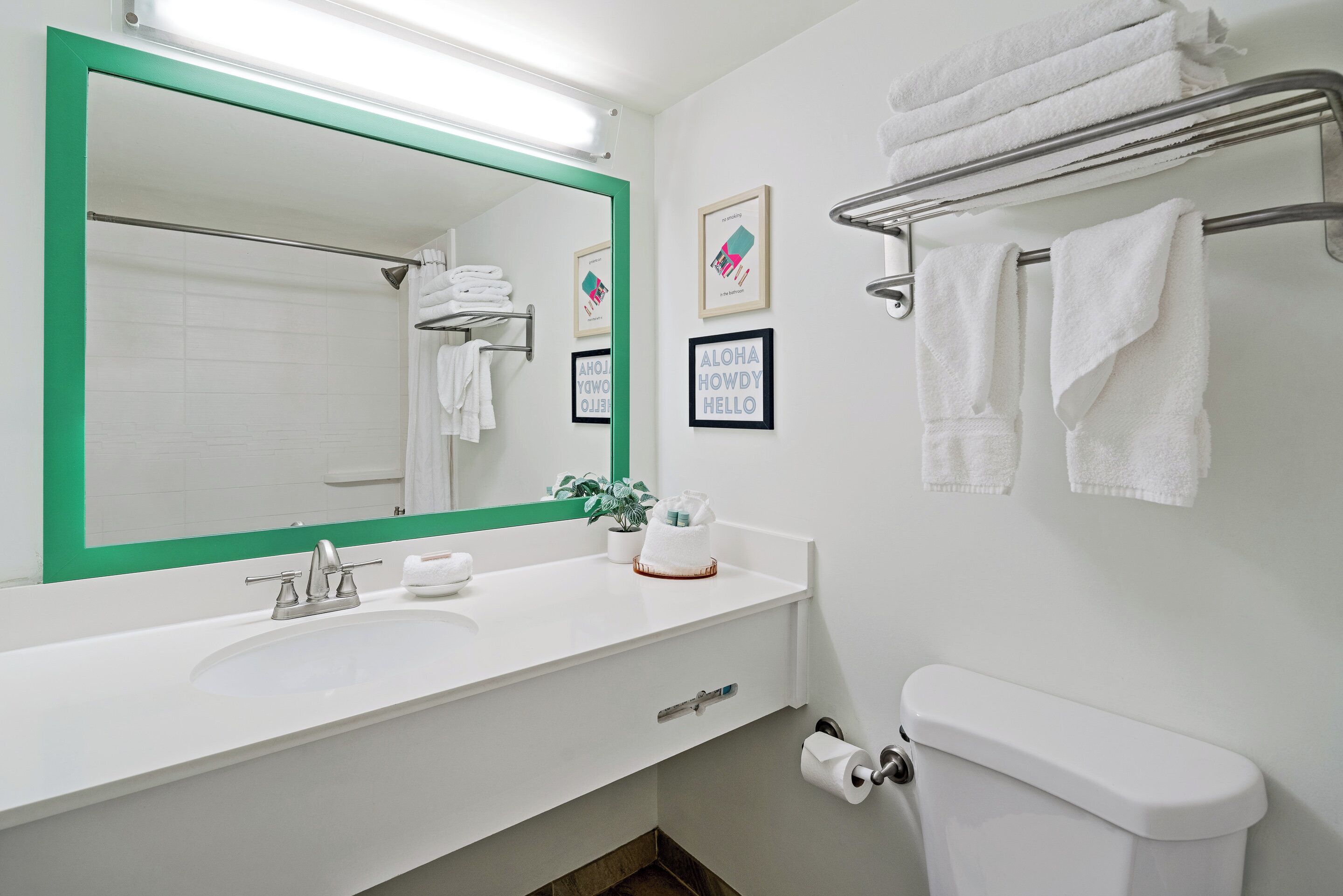 A modern bathroom with a white sink, green-framed mirror, white toilet, and towel rack.