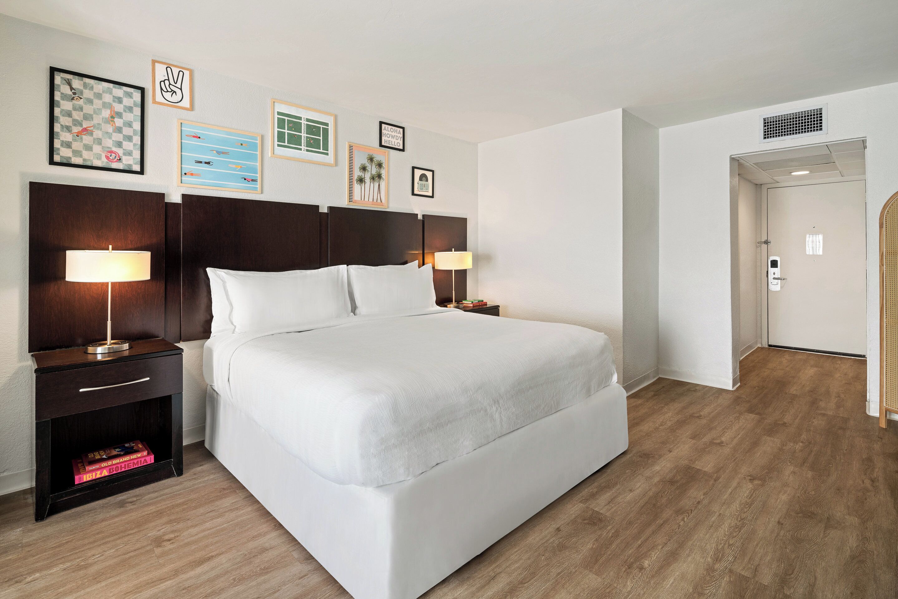 Camera d'albergo ordinata con un letto grande, due comodini con lampade e una porta che conduce al bagno.